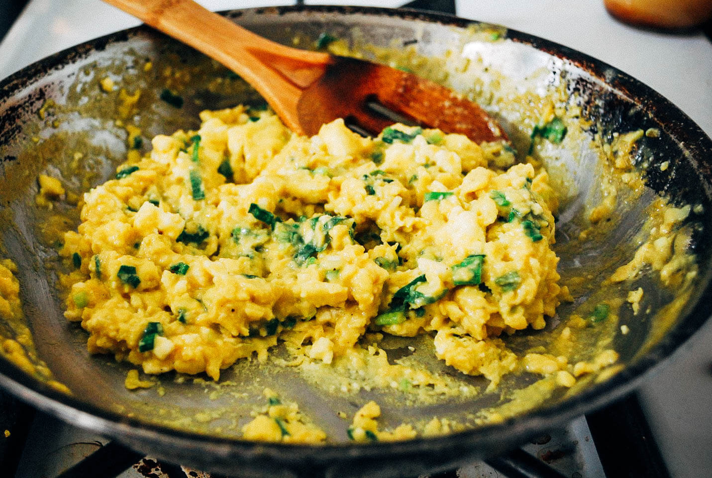 Slow-cooked scrambled eggs require patience, but reward the eater with exceptional flavor. These slow-cooked scrambled eggs are mixed with ricotta, Parmesan, garlic scapes, and spring onions, but feel free to add whatever cheese and alliums you may have on hand. 