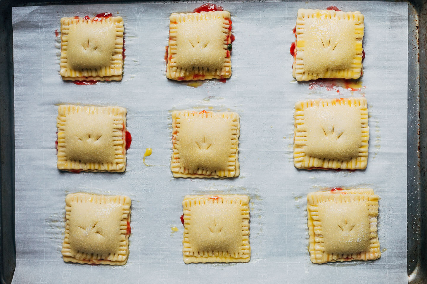 Nine square hand pies arranged on a baking sheet lined with white parchment paper.