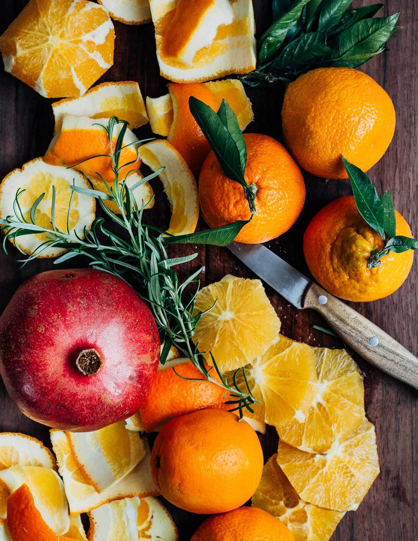 A cutting board with sliced oranges and mandarins, and a whole pomegranate. 