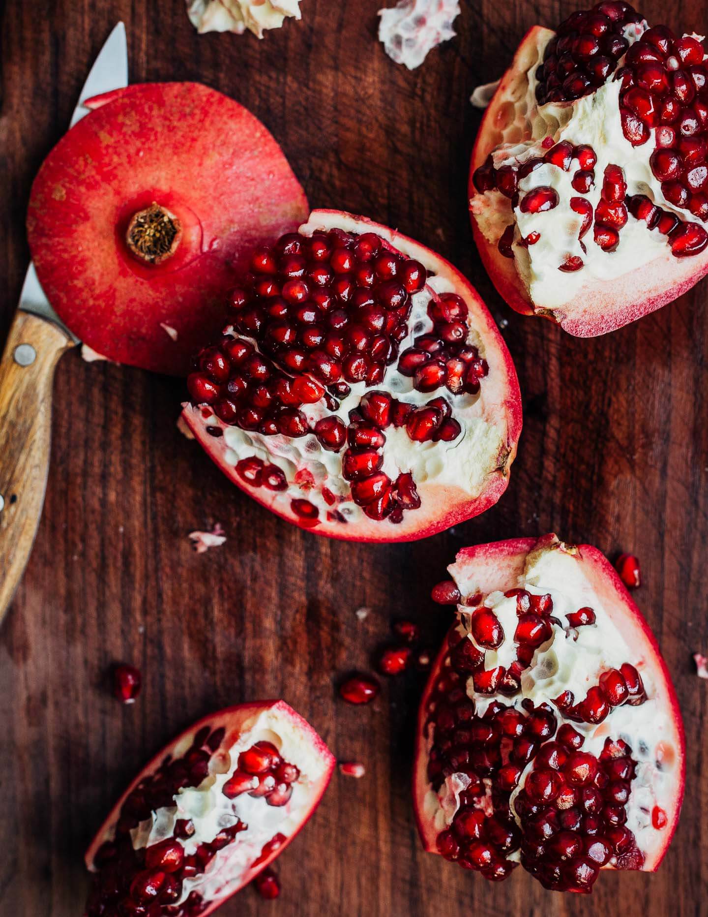 A whole pomegranate, split apart on a cutting board. 