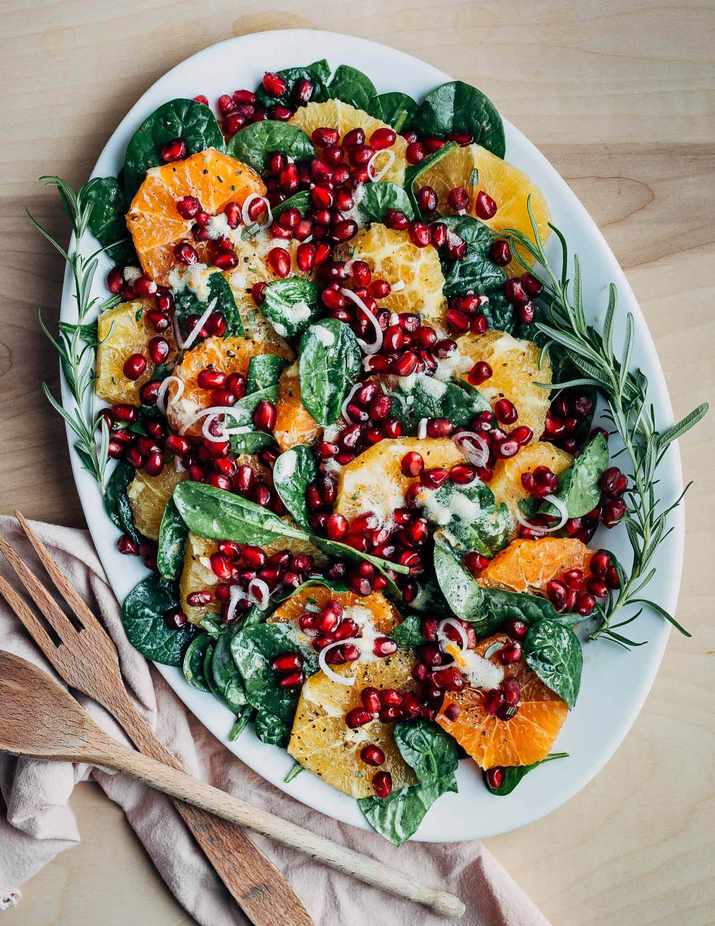 An orange and pomegranate salad on a big platter with serving utensils alongside. 