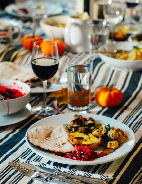 A crowded table set for Thanksgiving with lots of sides and loaded plates. 