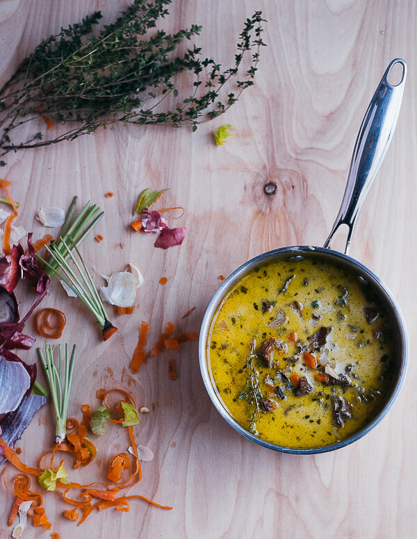 A sauce pan filled with soup and surrounded by carrot tops and peels. 
