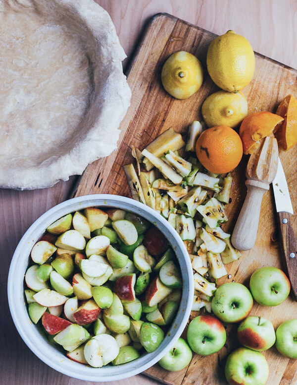 A cutting board with prepped apples and a pie shell, just about to be filled. 