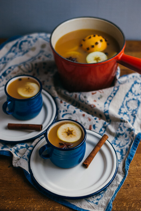 A small pot and two mug of hot apple cider.