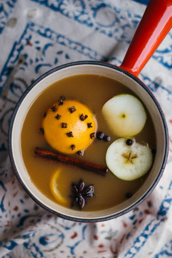 A pot of spiced apple cider with a pomander, apples slices, and spices. 