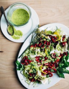 A platter with a cherry and fennel caprese salad alongside a little bowl of dressing.