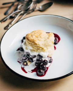 A serving of blueberry shortcake on a plate, with the blueberry filling oozing out.
