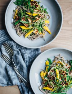 Two bowls filled with soba noodles and mangoes