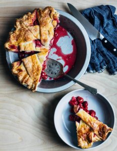 A cherry pie cut into slices with one slice sitting on a plate.