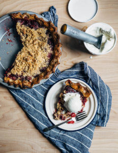 A cherry crumb pie with several slices cut out with one of the slices served on a plate with ice cream.