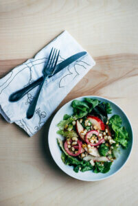 A bowl of charred corn and salad greens.