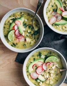 Three bowls filled with pozole verde and toppings.
