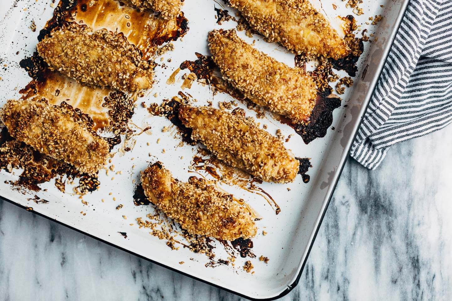 A healthful, Whole30-compliant avocado and mandarin orange salad topped with crisp sesame-crusted baked chicken tenders and drizzled with a creamy mandarin-ginger dressing.