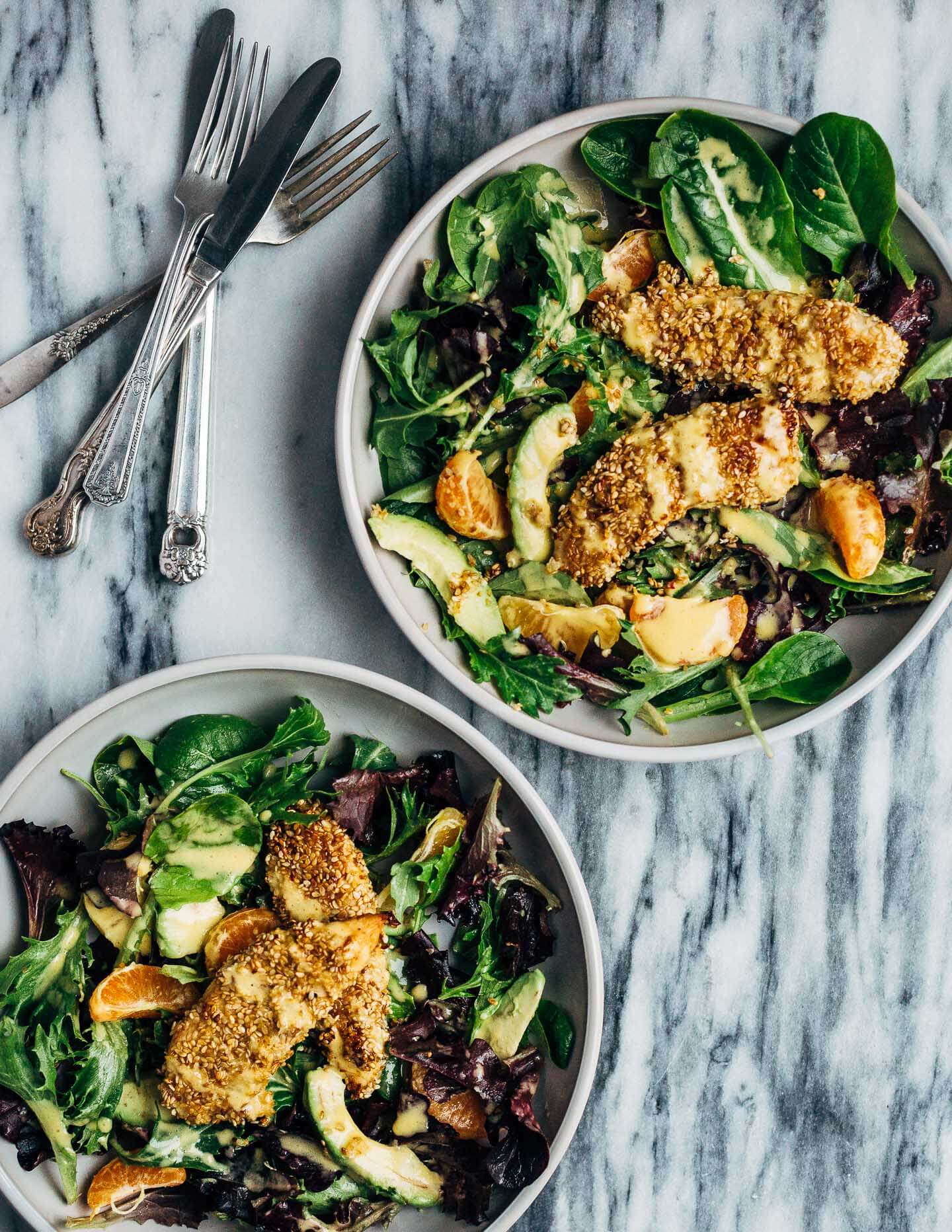 A healthful, Whole30-compliant avocado and mandarin orange salad topped with crisp sesame-crusted baked chicken tenders and drizzled with a creamy mandarin-ginger dressing.