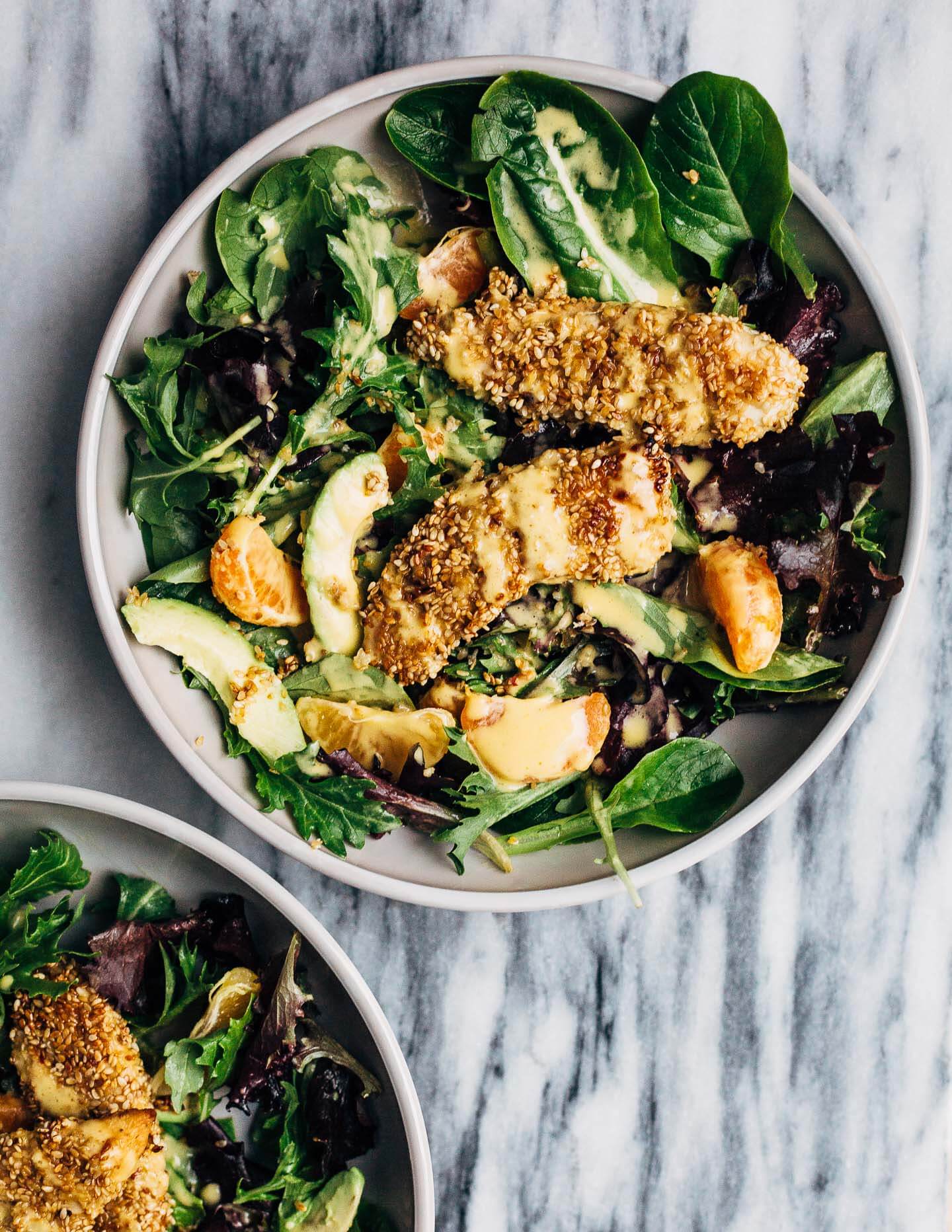 A healthful, Whole30-compliant avocado and mandarin orange salad topped with crisp sesame-crusted baked chicken tenders and drizzled with a creamy mandarin-ginger dressing.