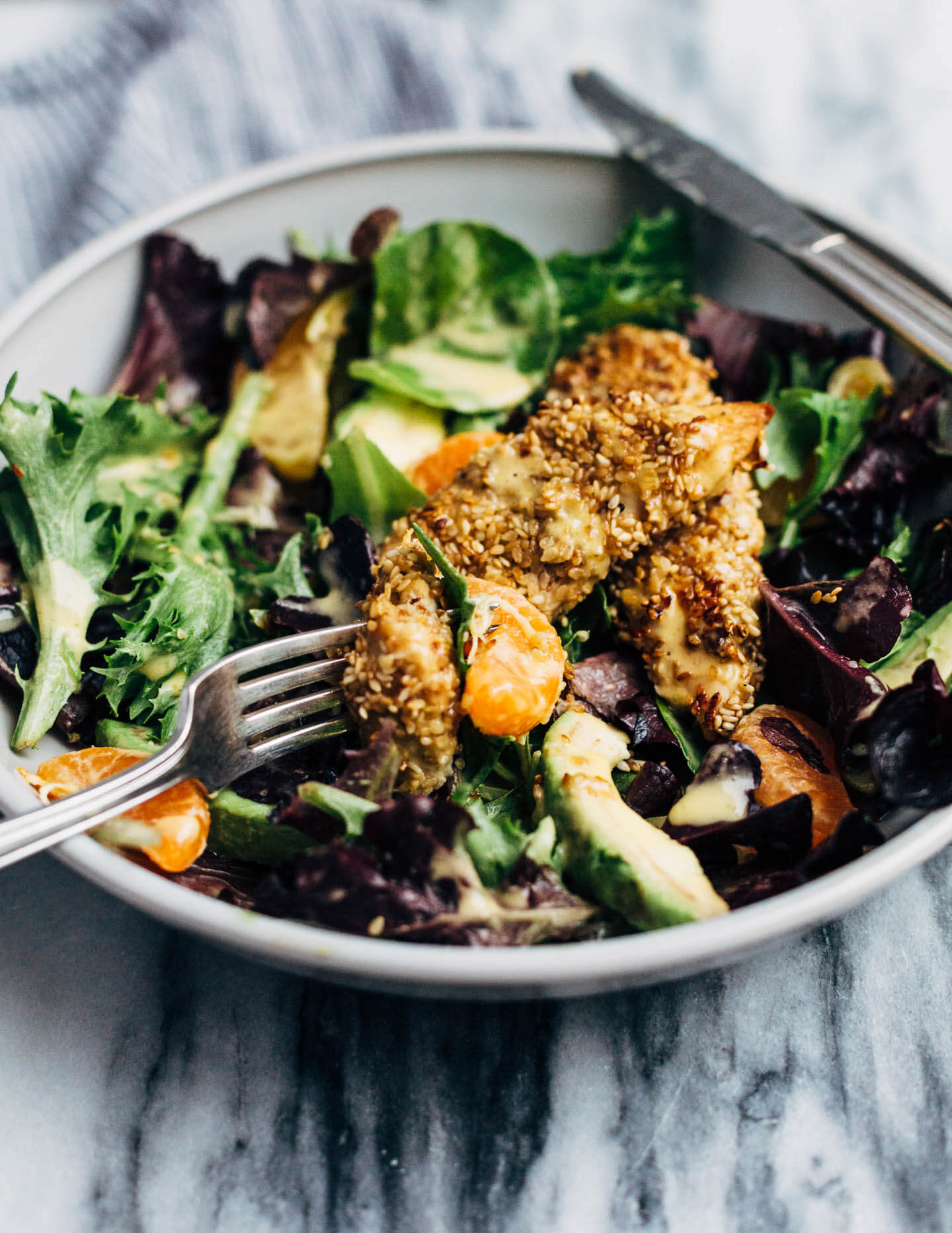 A healthful, Whole30-compliant avocado and mandarin orange salad topped with crisp sesame-crusted baked chicken tenders and drizzled with a creamy mandarin-ginger dressing.