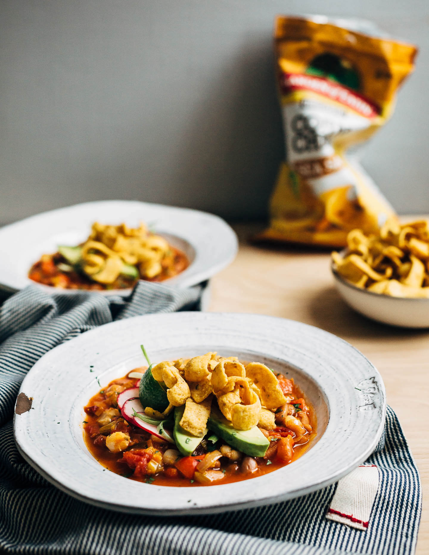 Hearty pinto bean chili with a flavorful tomato base flecked with leeks, chili peppers, and hominy and topped with fresh cilantro, lime, sliced avocado and radish, and crunchy corn chips. 
