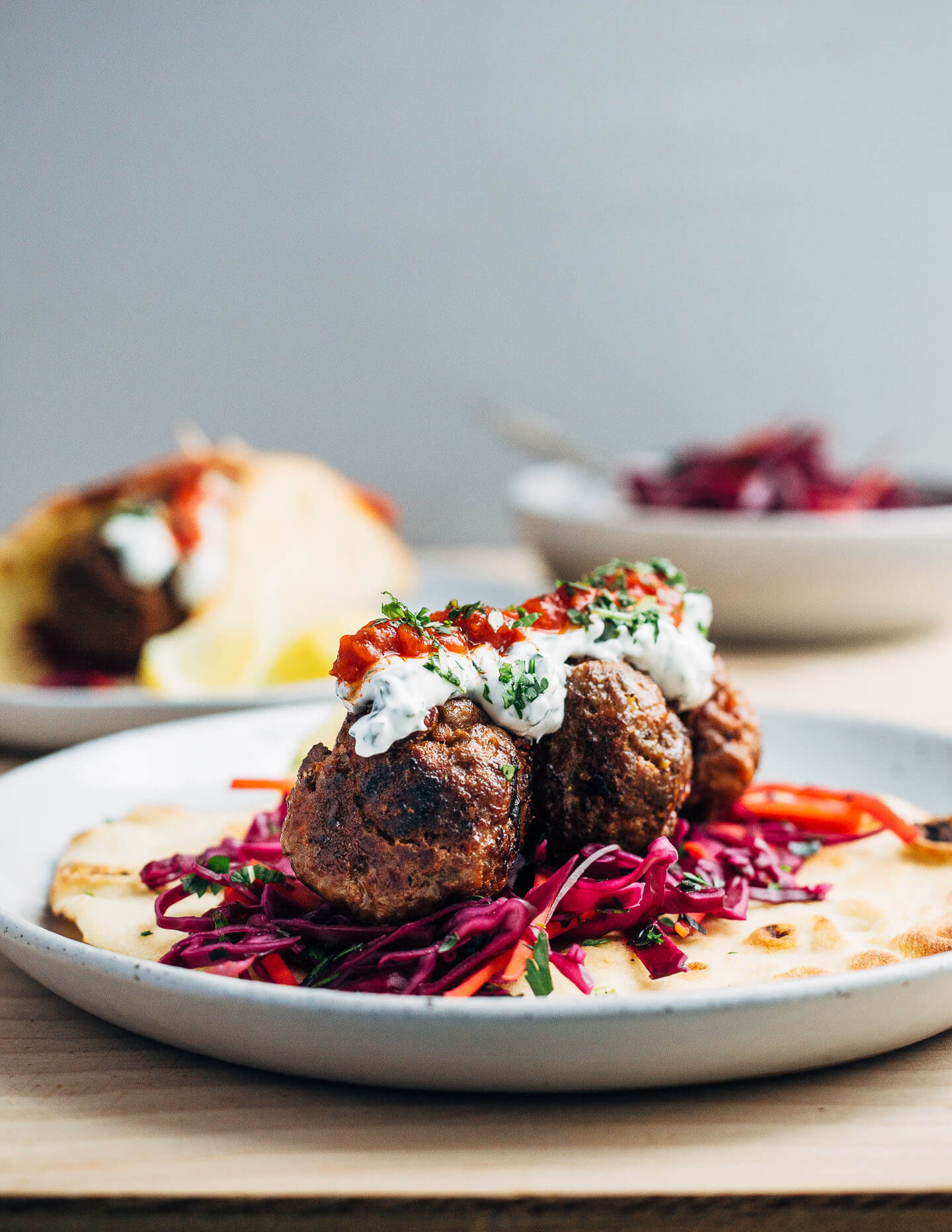 Exceptionally delicious merguez meatball flatbreads layered with red cabbage slaw, herbed yogurt, and harissa. 