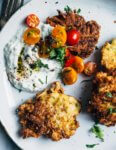 Crispy-edged summer squash fritters – imbued with the distinctive flavors of toasted cumin and fried black mustard seeds – are an unexpected and delicious way to make use of summer squash stores. The fritters are served with a cooling green onion and cilantro raita and sweet cherry tomatoes.