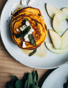 A plate with pancakes topped with sage and goat cheese.