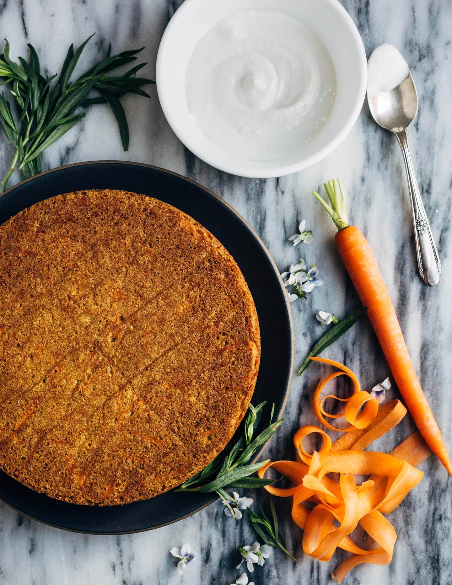 A simple olive oil carrot cake for spring celebrations! The tender, springy whole wheat crumb is suffused with nutty olive oil, fresh carrots, and orange zest. The cake is topped with an airy, lightly sweet yogurt and cream cheese frosting, carrot ribbons, tarragon, and edible flowers. 