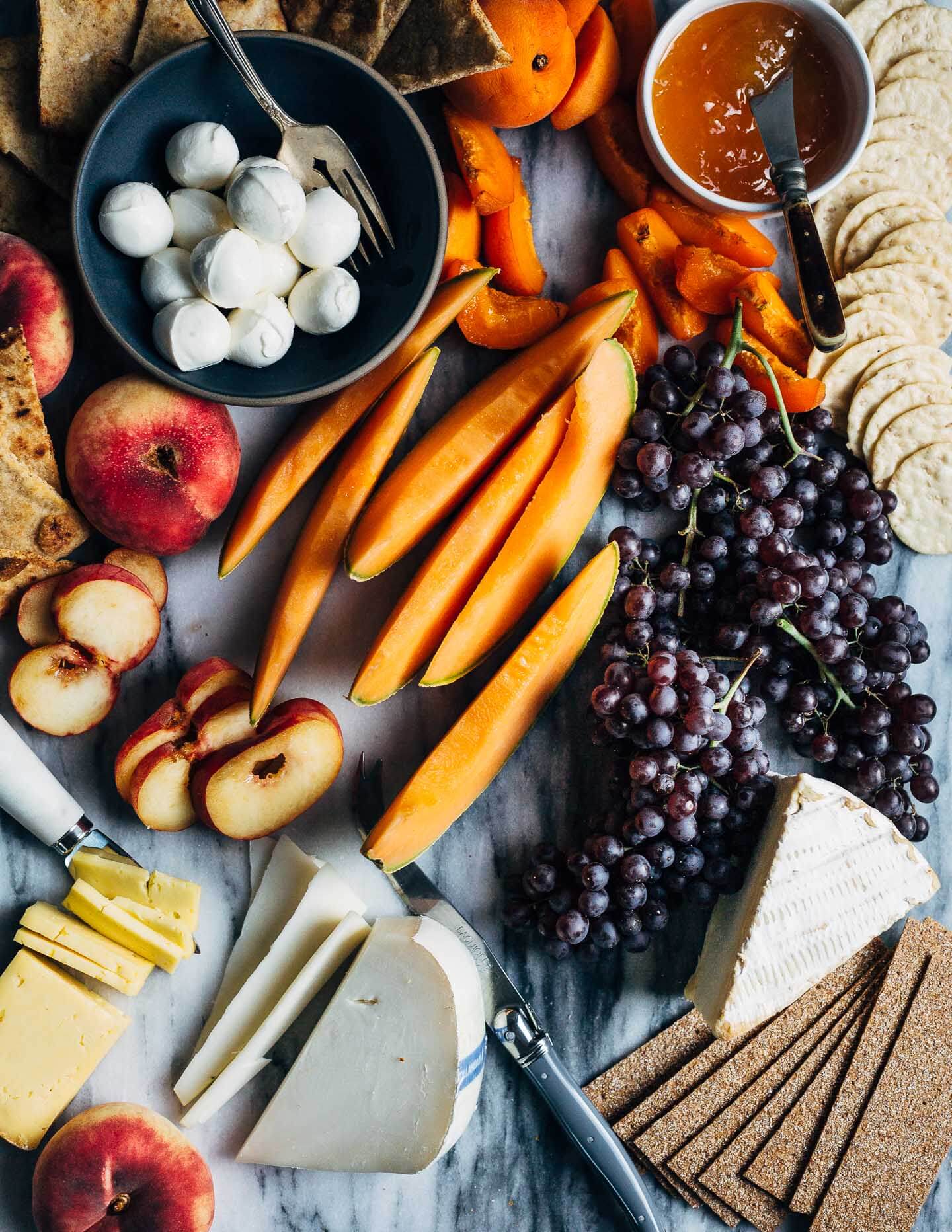 A simple summer fruit and cheese board featuring delicate goat and cow's milk cheeses paired with fresh cantaloupe, apricots, peaches and grapes.