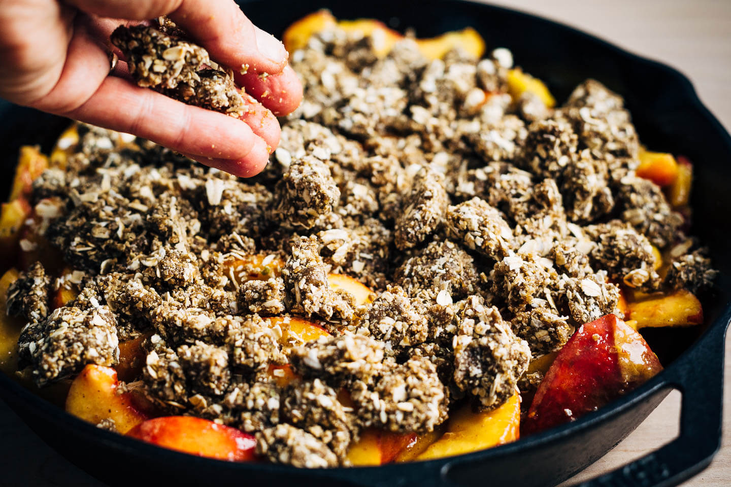 Adding crumble topping to a vegan peach crumble. 