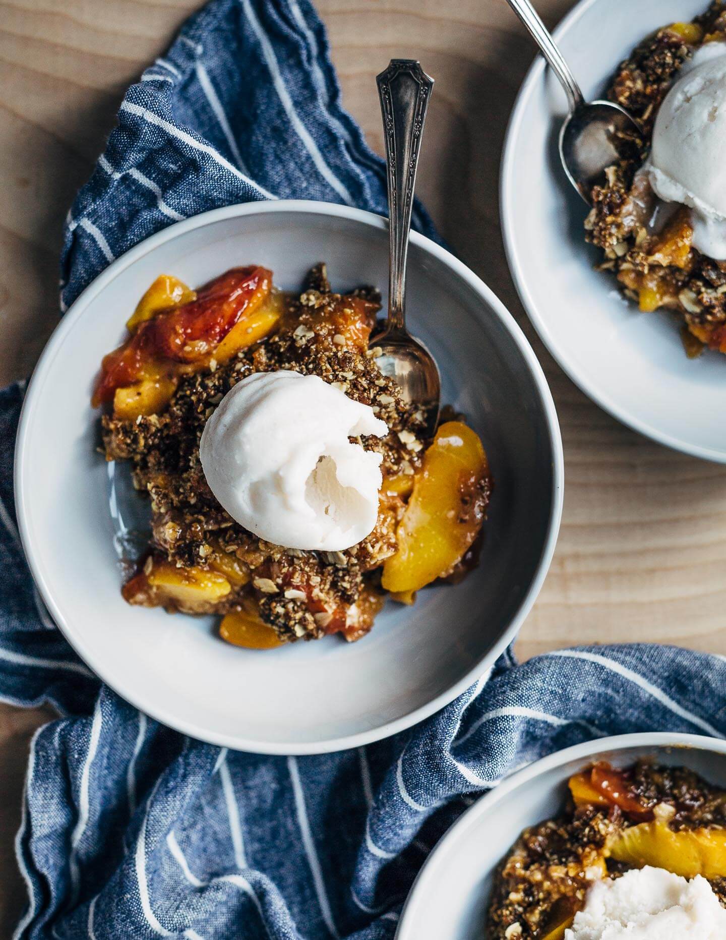 This intensely flavorful gluten-free, vegan peach crumble with masala chai-spiced coconut sorbet is the perfect summer baking project. Big flavors like cardamom, ginger, and cinnamon lend zip to creamy homemade coconut sorbet – an ideal counterpoint to chewy, molasses-infused seed and oat crumbles and bright peaches baked with a host of fragrant spices.