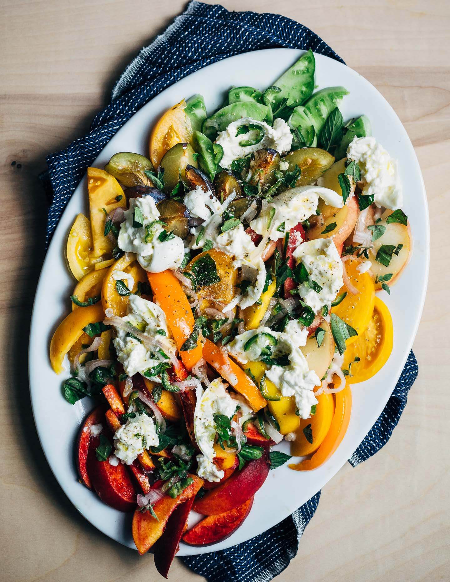 Peak summer ingredients speak for themselves in this layered stone fruit and tomato salad tossed with torn burrata, fresh garden herbs, and a spicy Serrano-lime dressing.