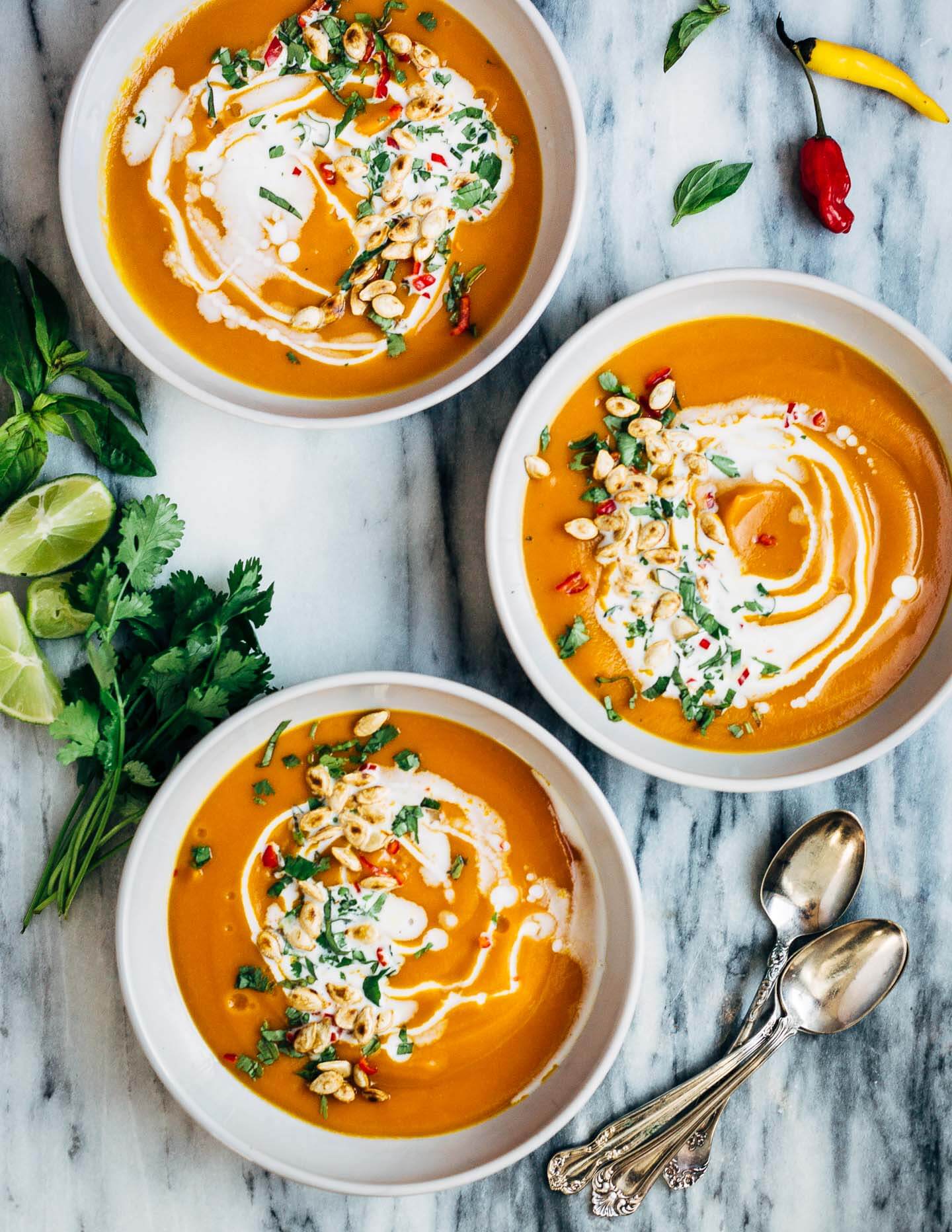 Vegan coconut curry winter squash soup drizzled with coconut milk and topped with fresh herbs and toasted squash seeds. 
