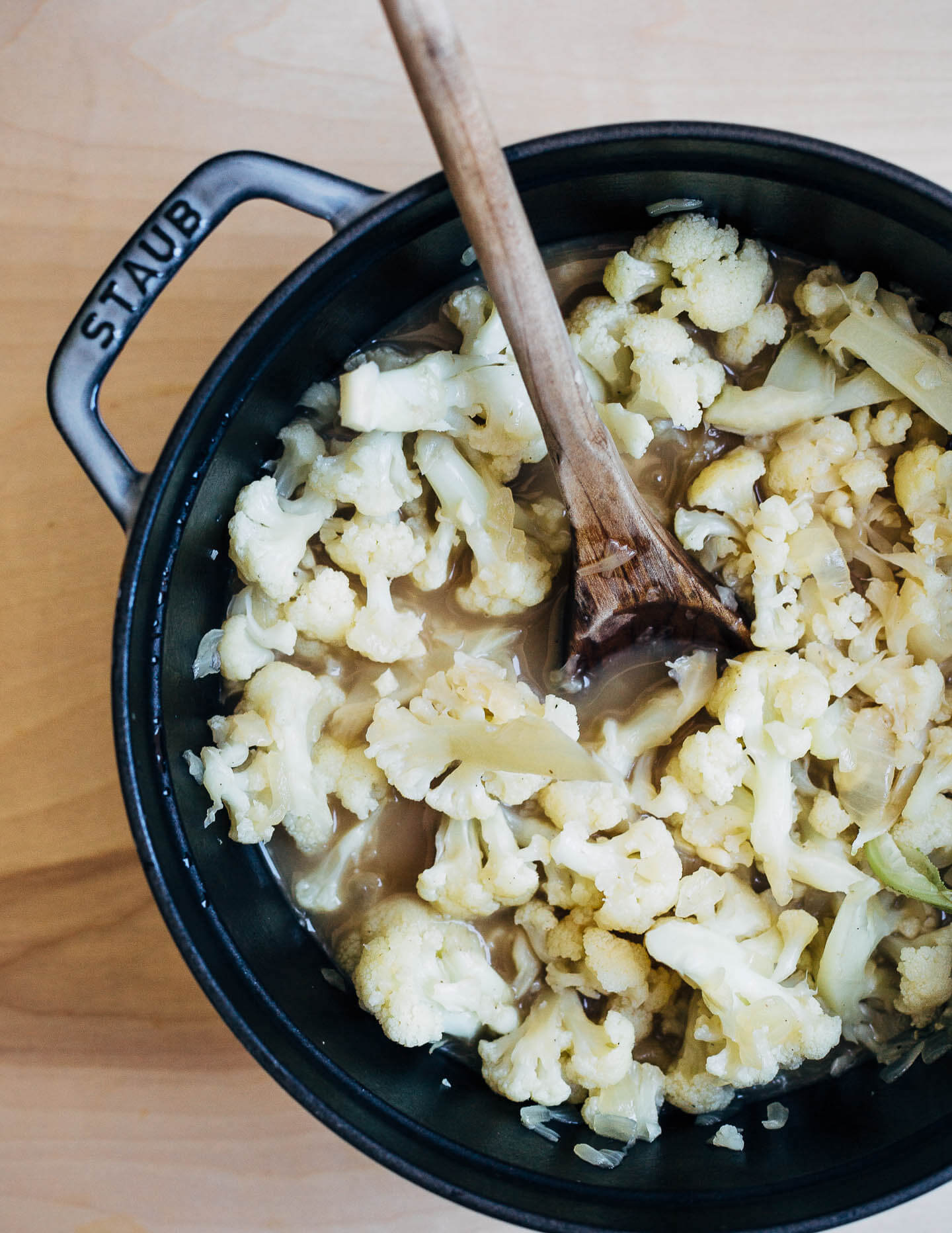 Cooking cauliflower in broth with sautéed onions.