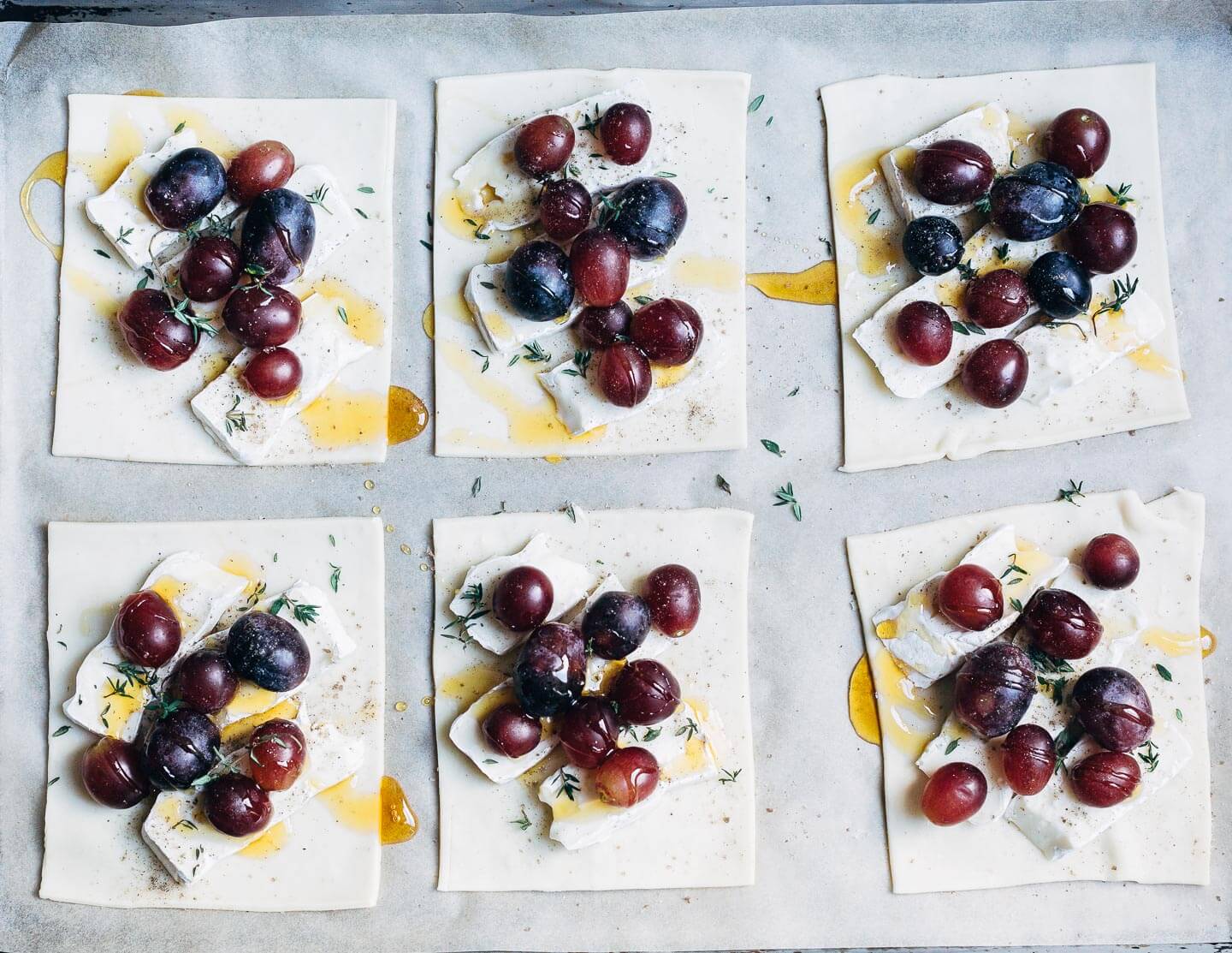 Puff pastry squares with brie, grapes, and thyme, ready for the oven.