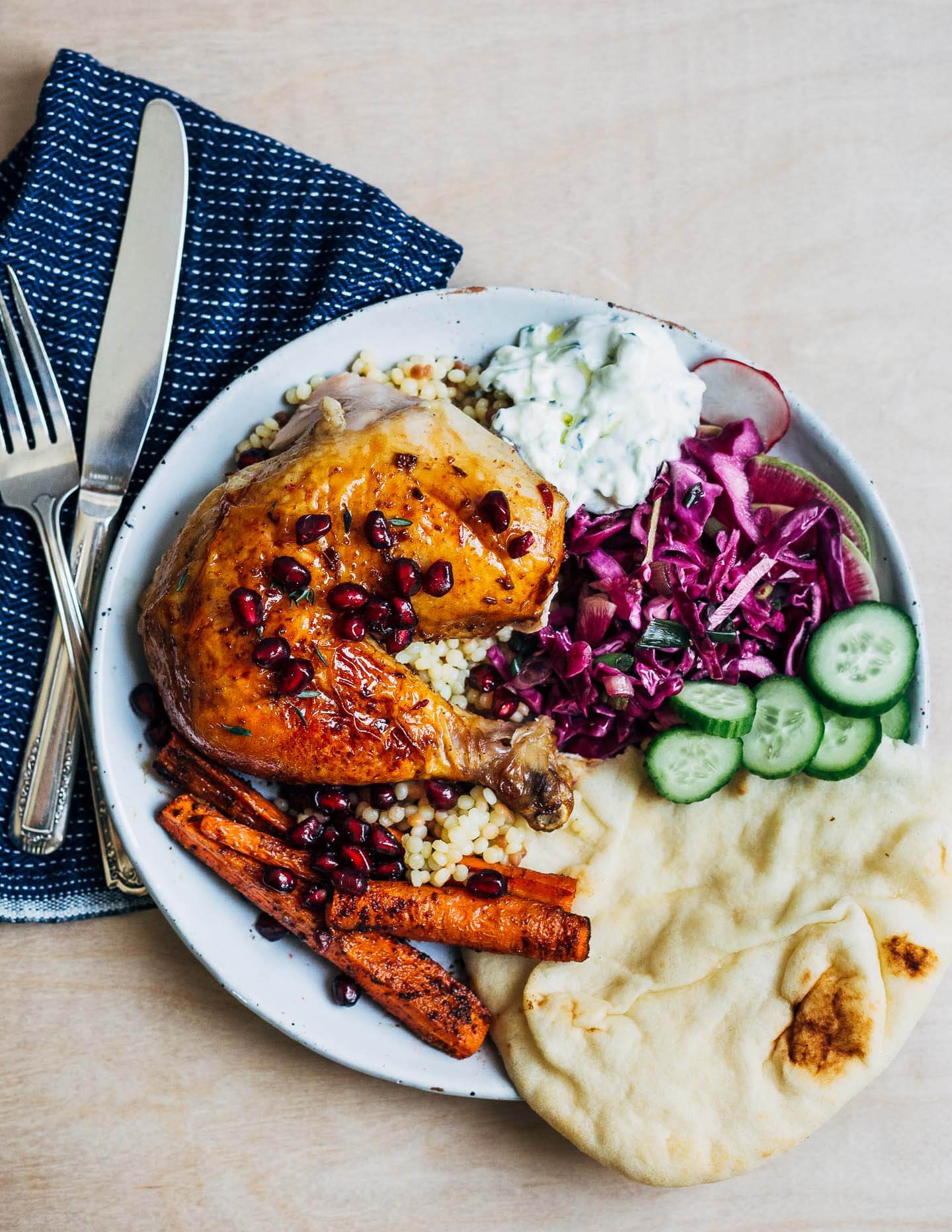 Pomegranate-glazed roasted chicken, plated with couscous, slaw, carrots, and tzatziki.