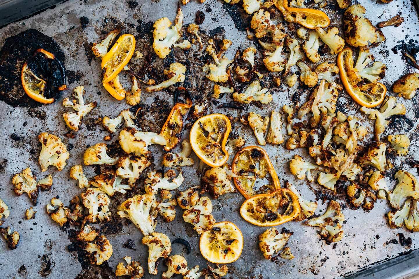 Roasted cauliflower and Meyer lemons on a tray. The cauliflower and lemons have deep brown edges and a warm hue. 