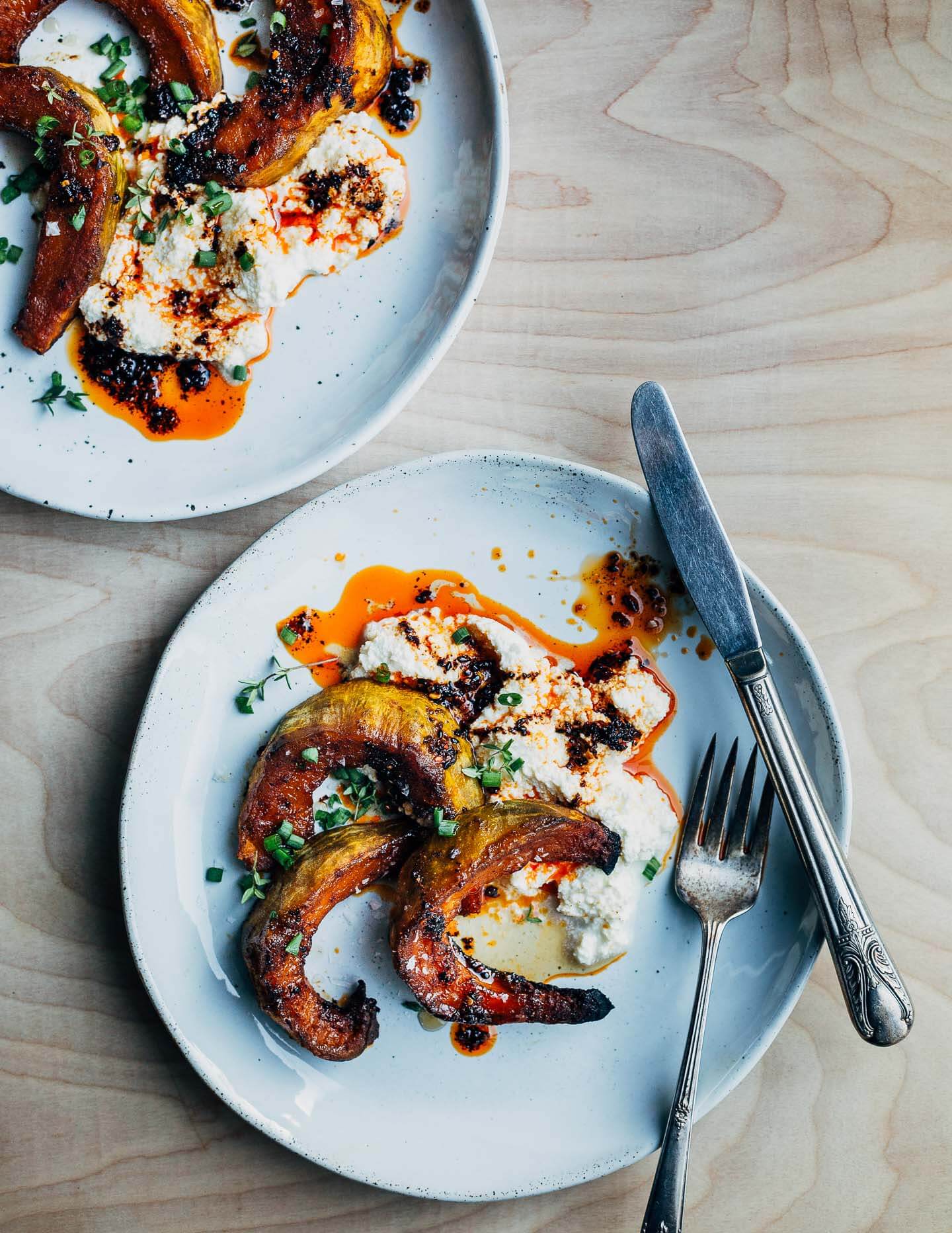 These savory sweet maple-roasted kabocha squash wedges are served with a dollop of creamy ricotta cheese, drizzles of maple syrup and chili oil, and flaky sea salt.