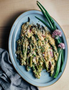 A platter with asparagus gratin and spring onions and chive blossoms alongside.
