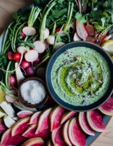 A platter filled with sliced radishes and a green dip in the center.