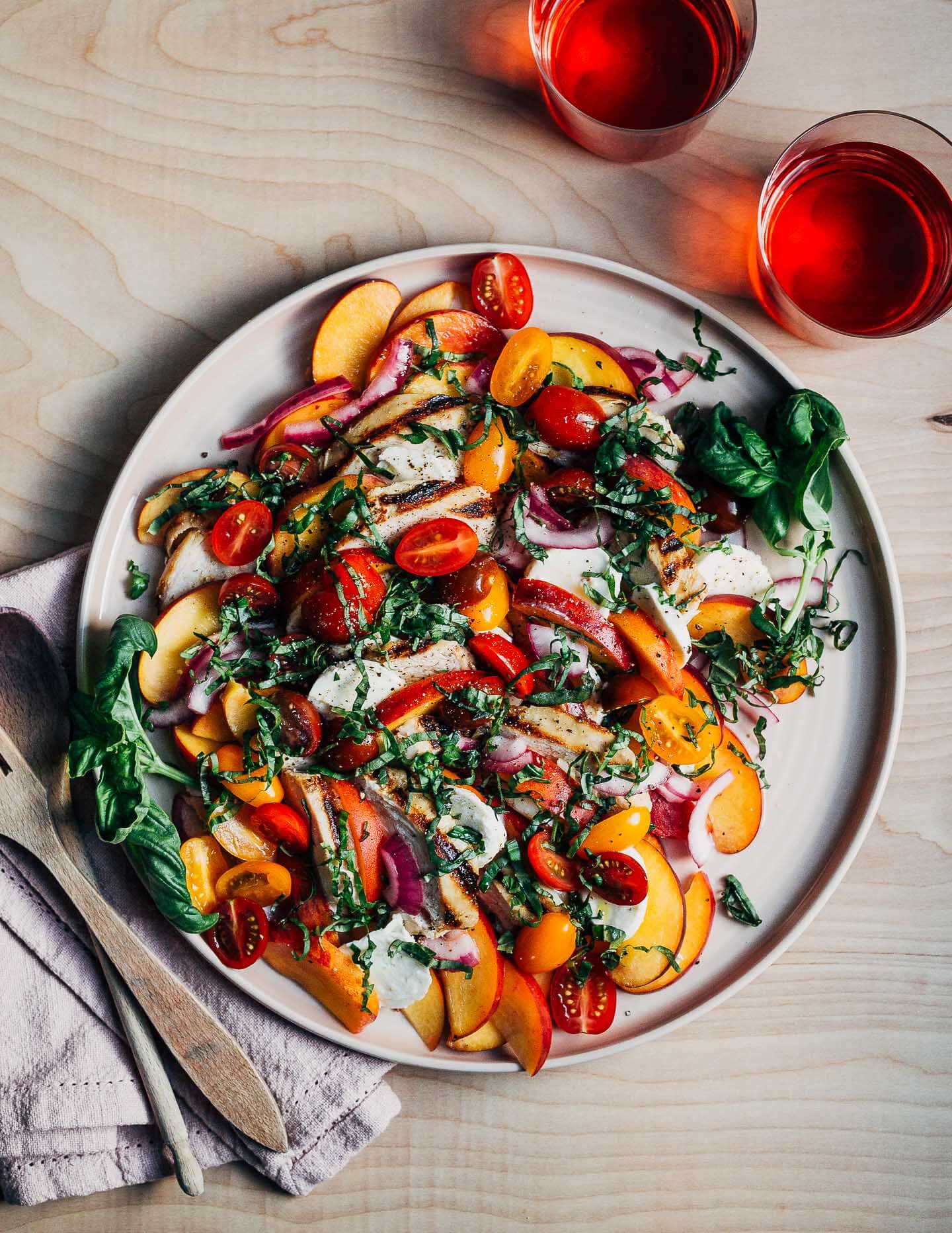 A platter with a grilled chicken caprese salad and two glass of pink cider.