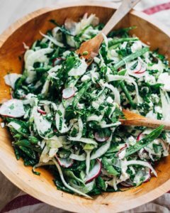 A wooden bowl with salad tongs and a shaved fennel and kale salad