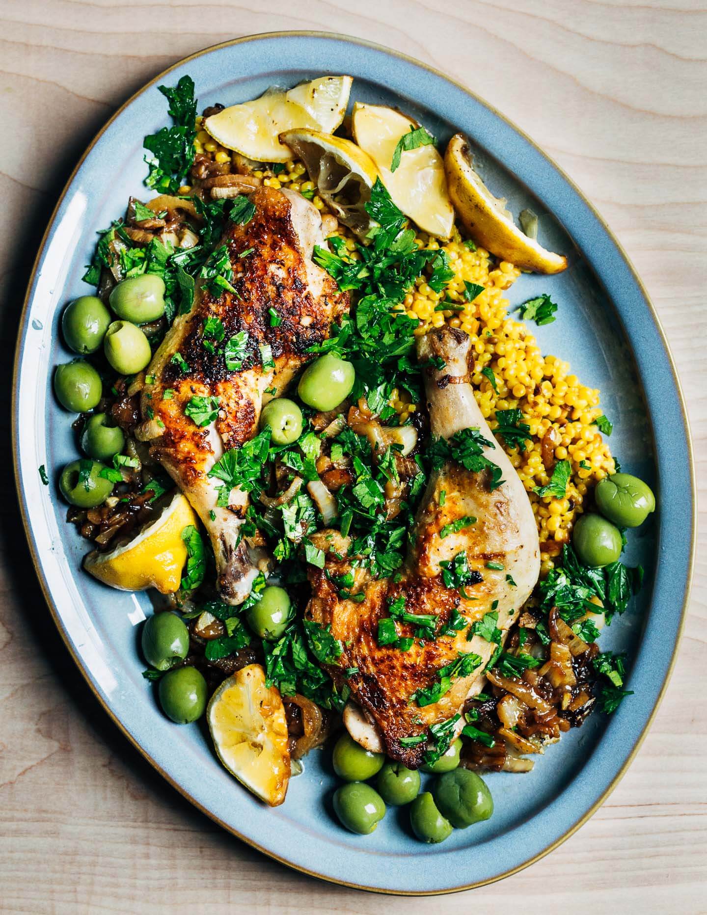 A platter with roasted chicken, couscous, olive, lemons, and herbs. 