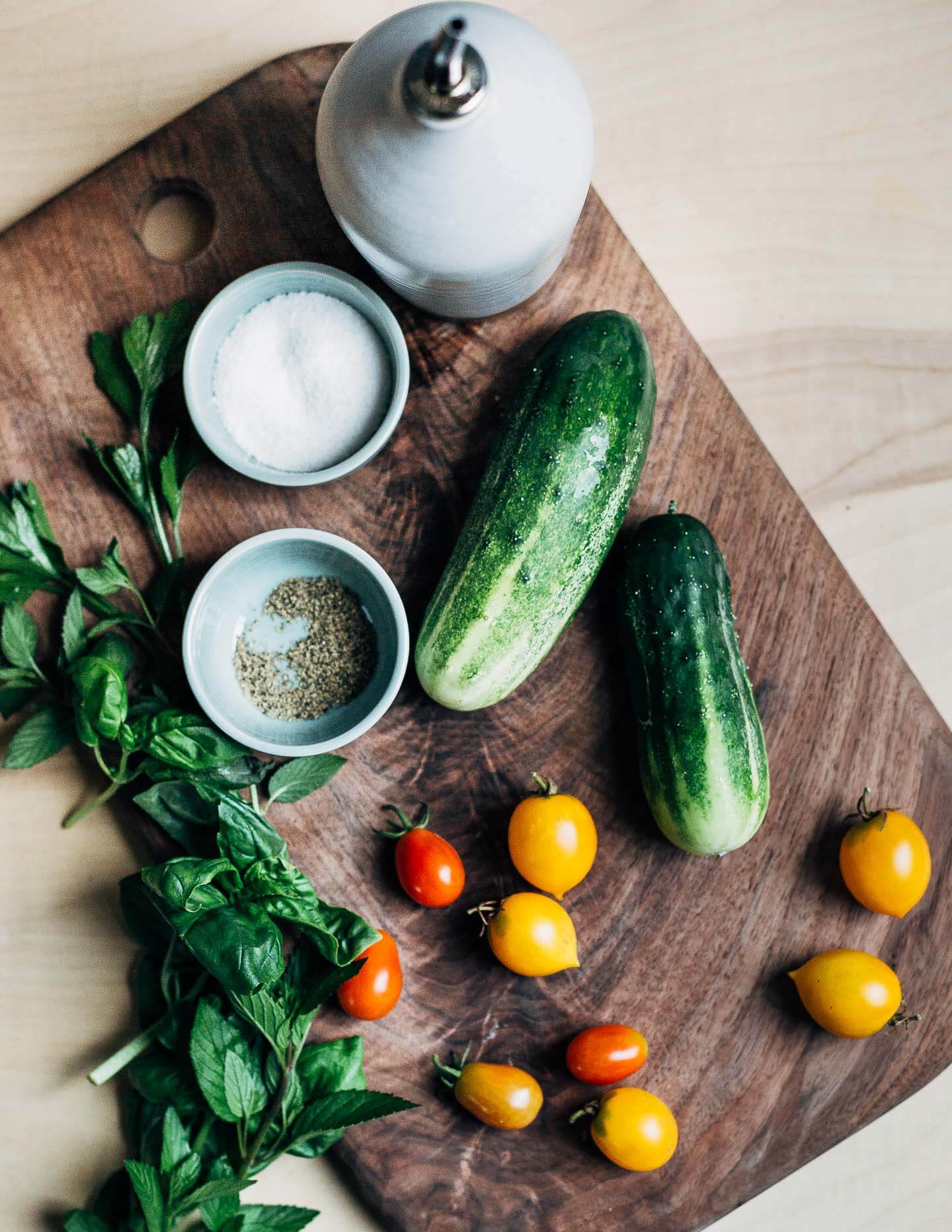 Vegetables and an olive oil dispenser on a cutting board.