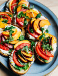 A platter with little toasts topped with ricotta, and sliced plums, nectarines, and tomtoes.