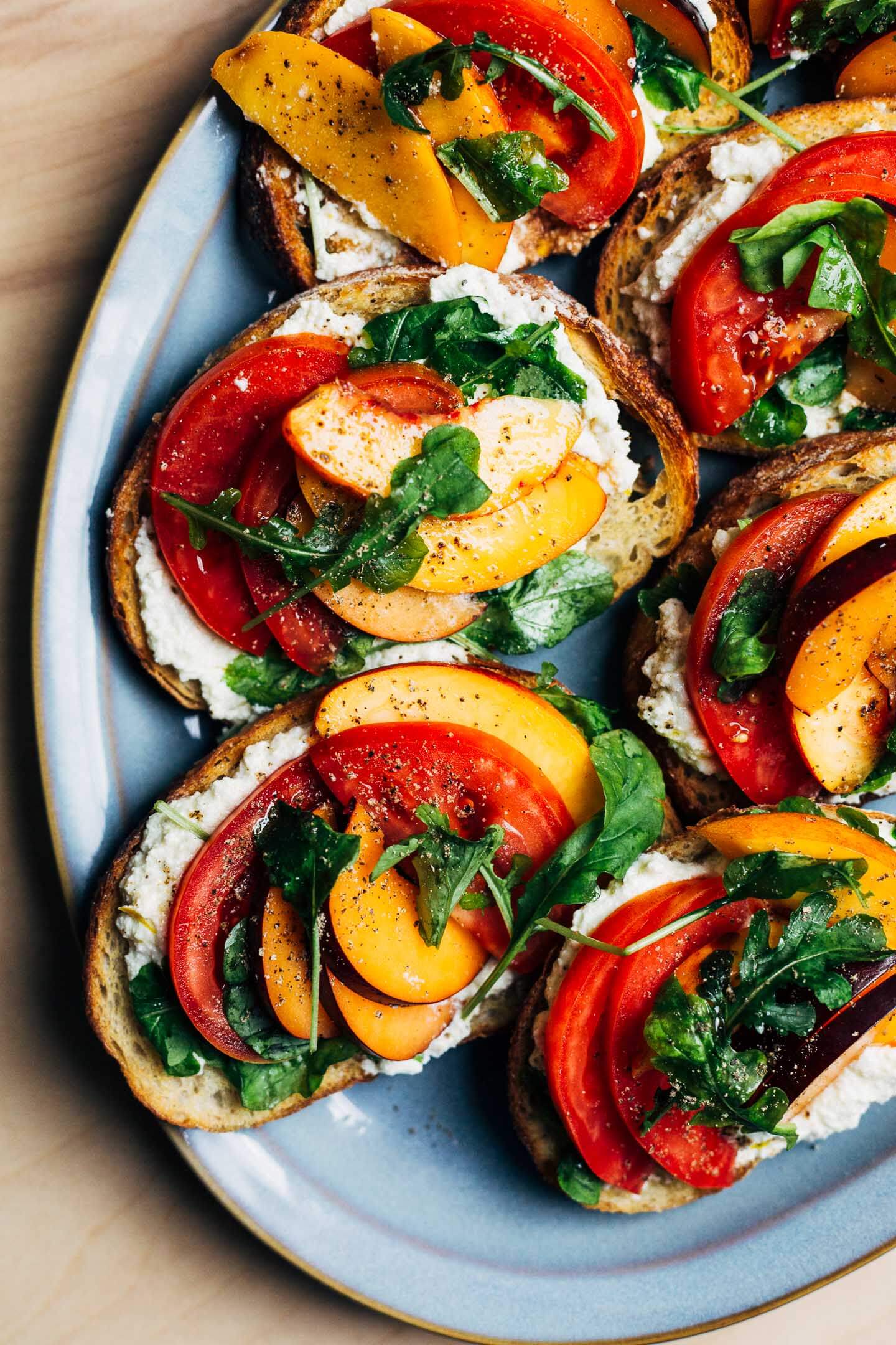 A platter with little toasts topped with ricotta, and sliced plums, nectarines, and tomtoes. 