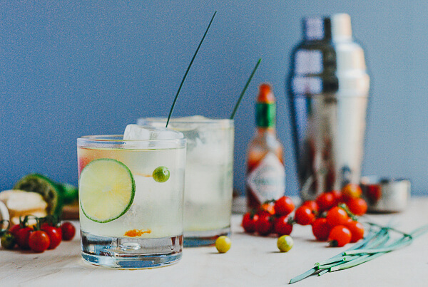 A table with two cocktails, cherry tomatoes and a cocktail shaker.
