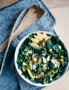 A bowl of kale salad with pears and goat cheese.