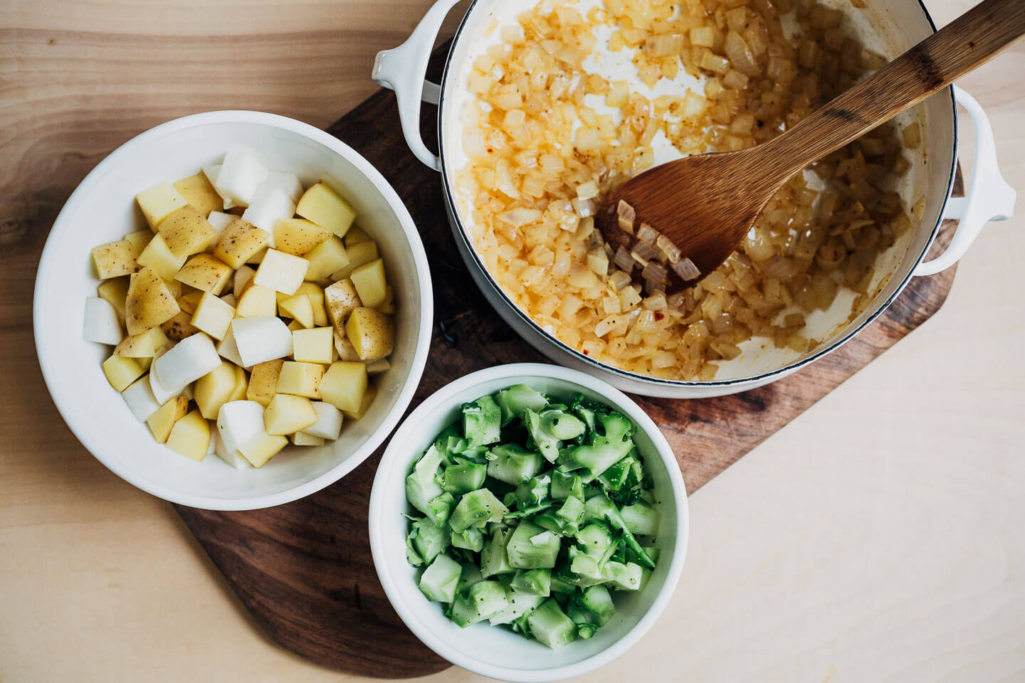 A soup pot with sautéed onions and bowls with potatoes and broccoli stems. 
