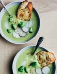 Two bowls of broccoli cheddar soup with croutons and sliced radish toppings.