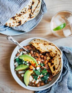 A bowl of pinto beans with avocado and a tortilla.