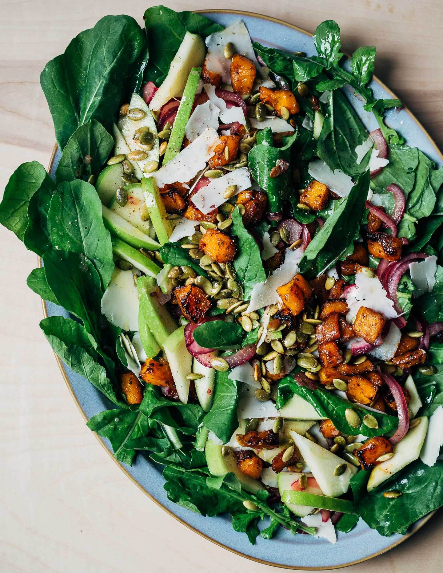 A platter of salad made with squash, pumpkin seeds, apples, and cheese. 